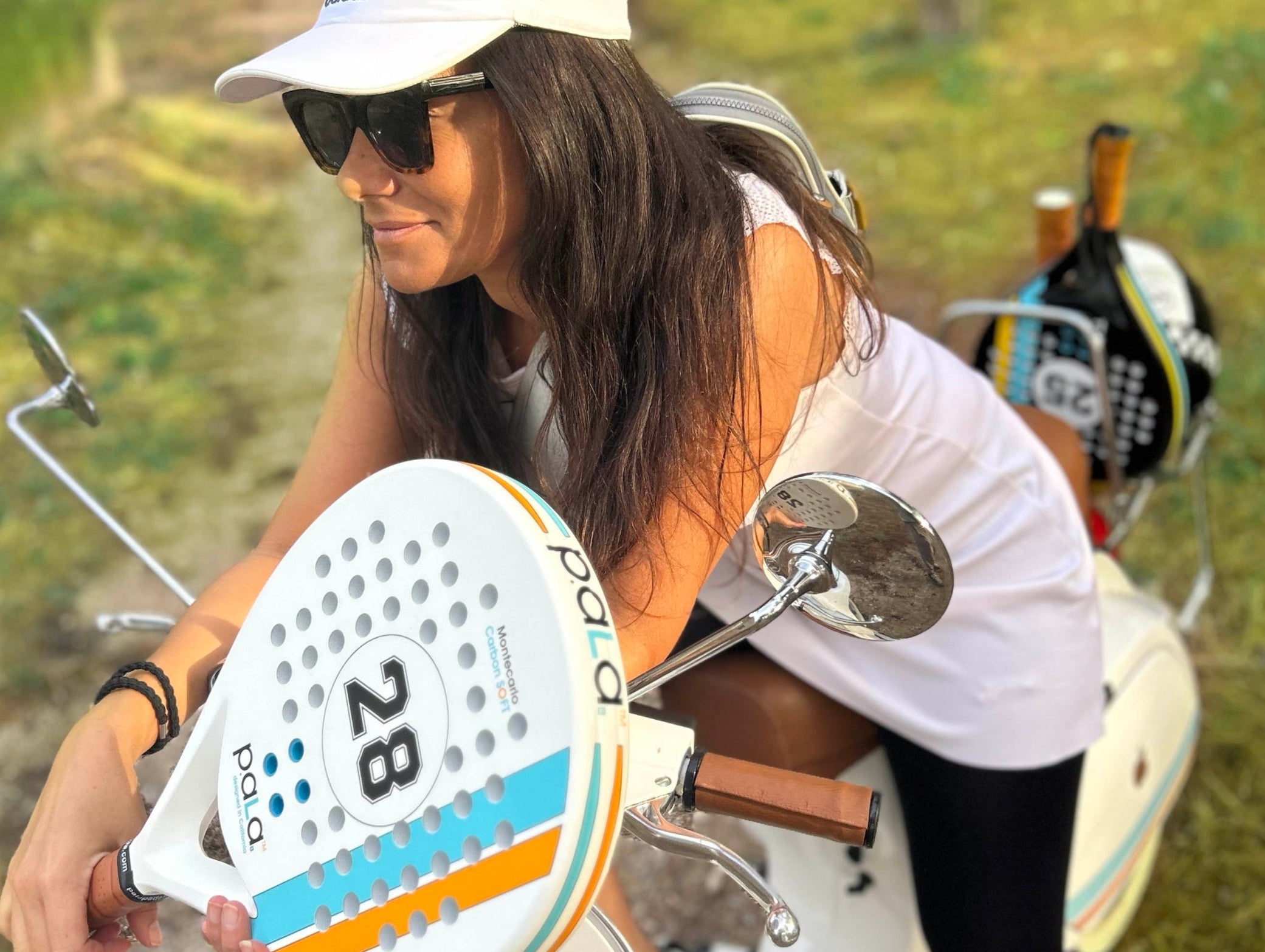 woman on a bike carrying a padel racket and a padel bag going to a padel court to play a padel game